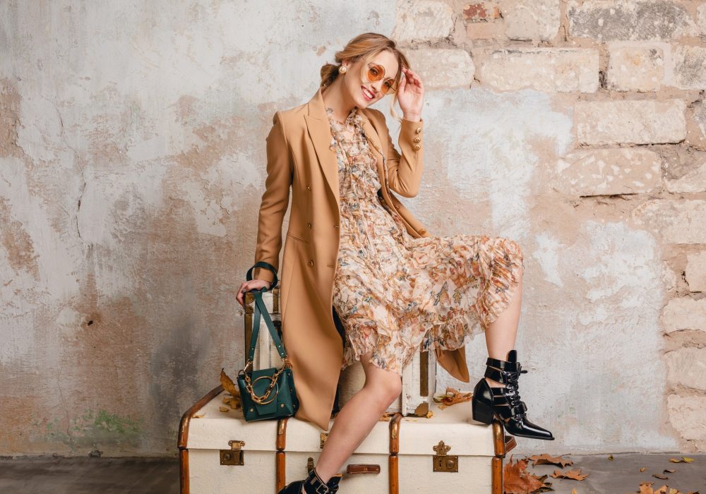 attractive-stylish-blonde-woman-beige-coat-sitting-suitcases-against-wall-street